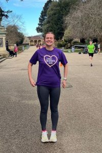 Laura smiling in a park wearing a Leeds Women's Aid tshirt