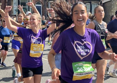 two girls wearing Leeds Women's Aid tshirts smiling whilst running in race